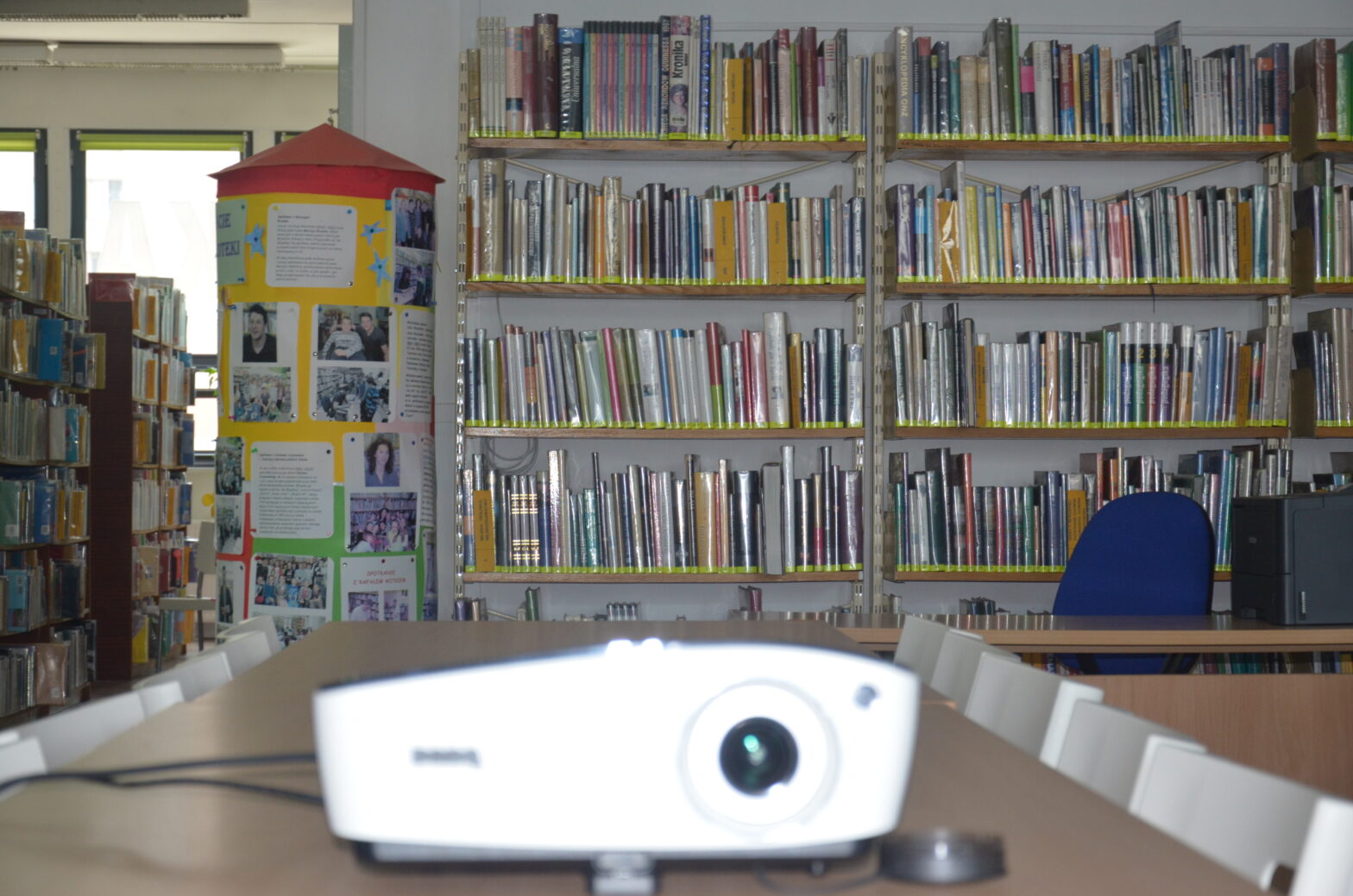 Na pierwszym planie rozmazany projektor, w tle regały biblioteczne wypełnione książkami