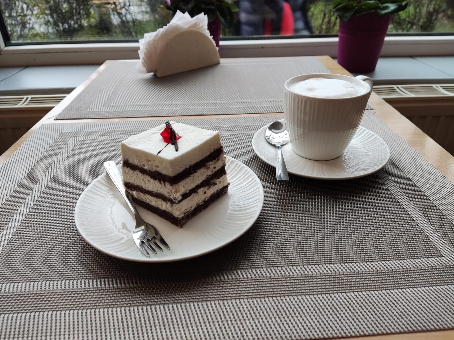 na talerzyku po lewej ciastko firmowe (taka namiastka torcika WZ) na talerzyku poprawej biała filiżanka z cappucino.